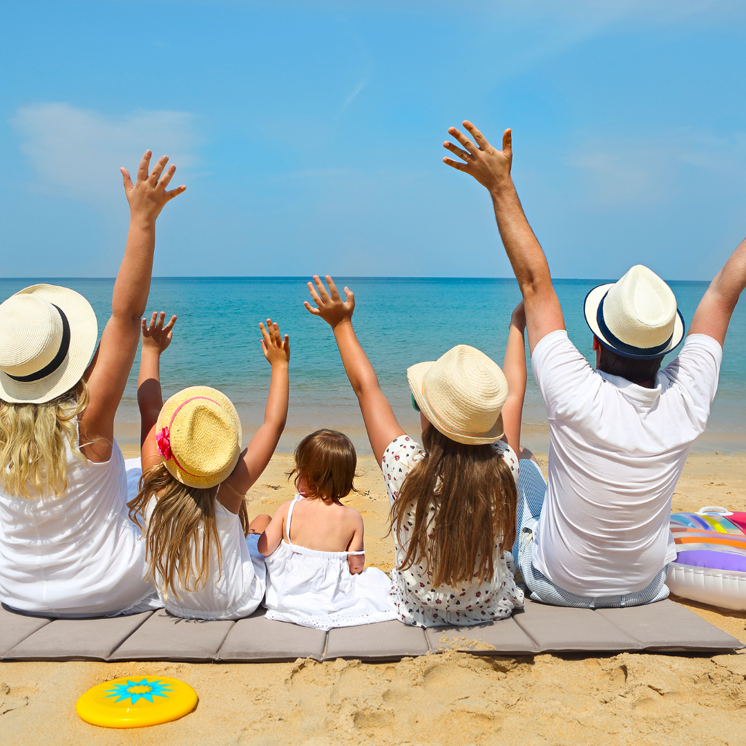 a family with children on a kid friendly vacation sitting on a beach, with their hands in the air.