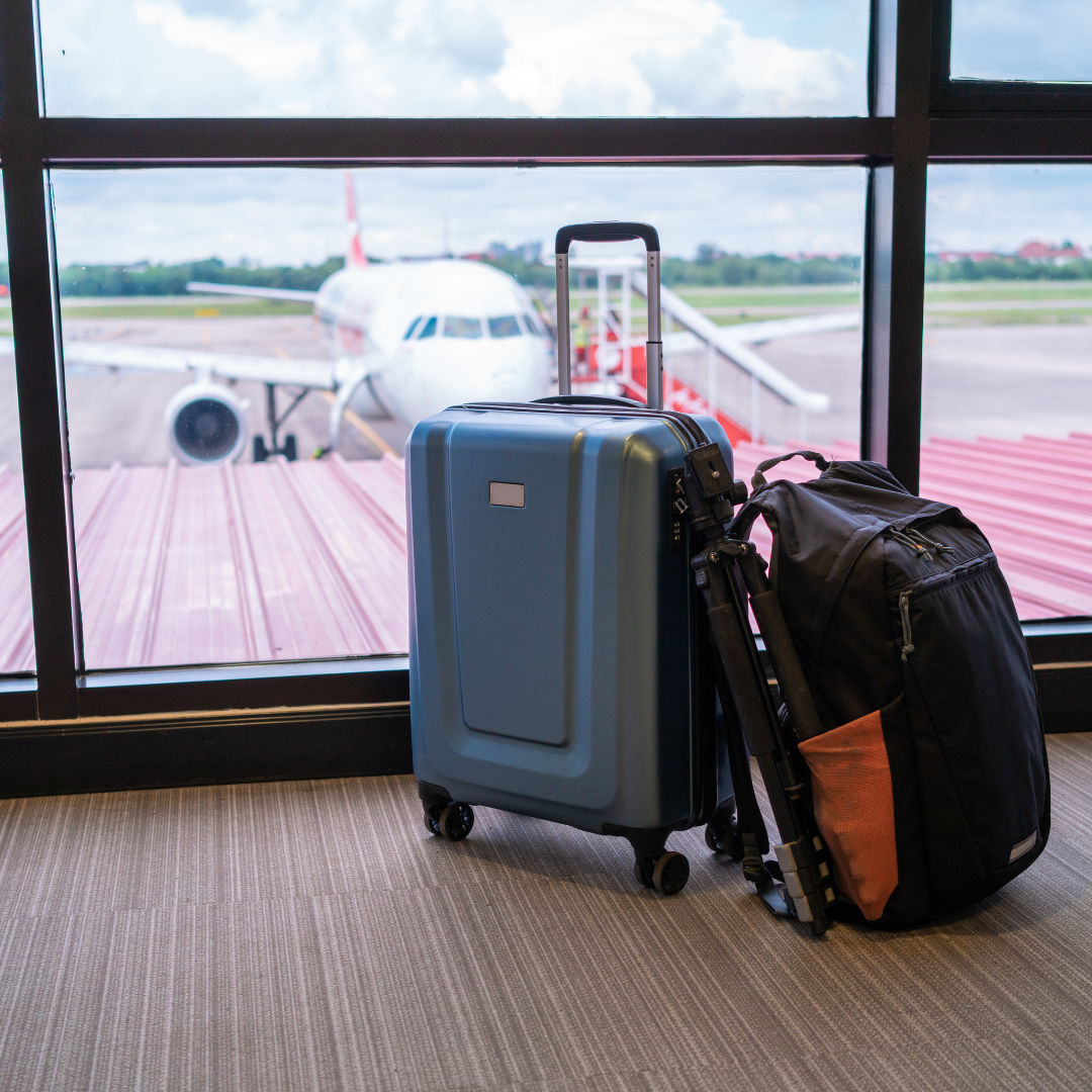 suitcase and backpack in airport terminal with airplane in the background.