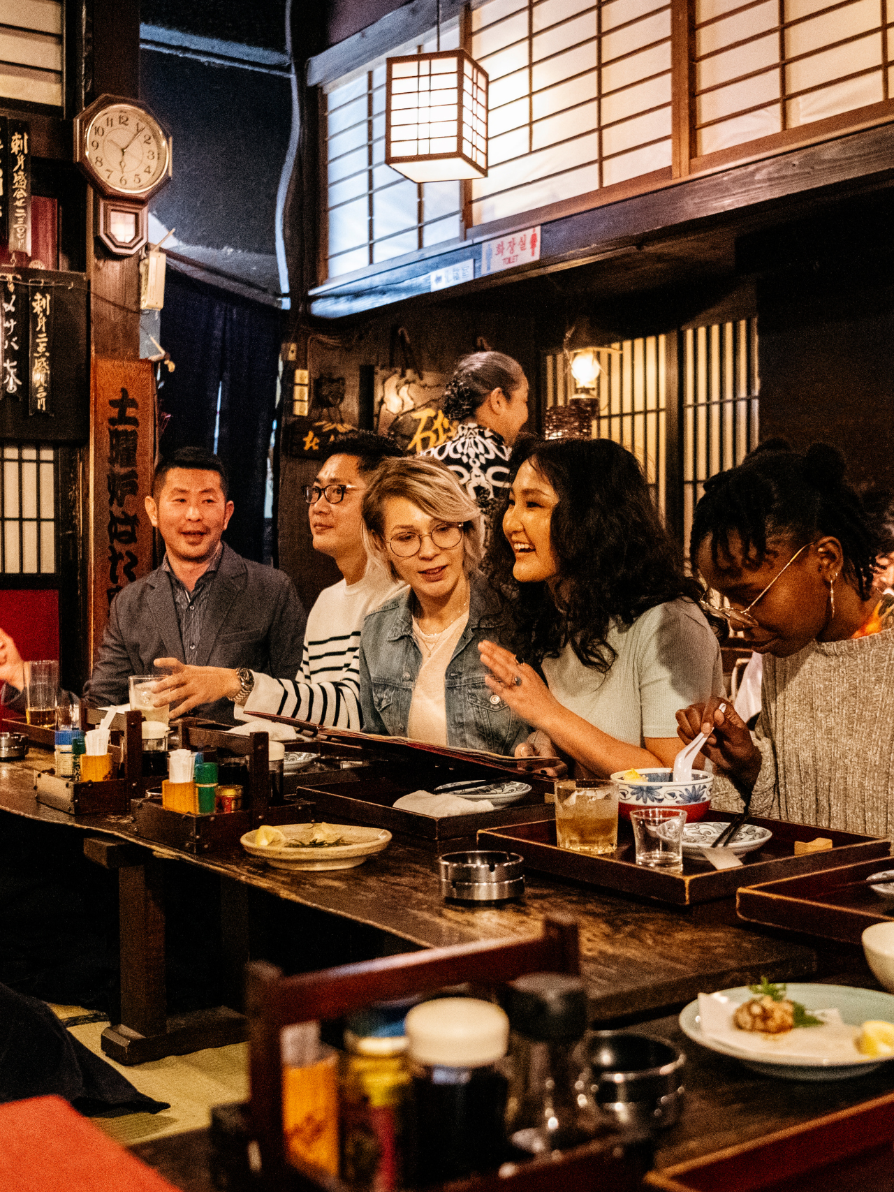 Group of friends ordering food in Japanese Izakaya. Waiter taking order from a happy friends, night out, drinking, and eating.