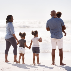 Family beach vacation. Rearview shot of young African American family standing on the beach.